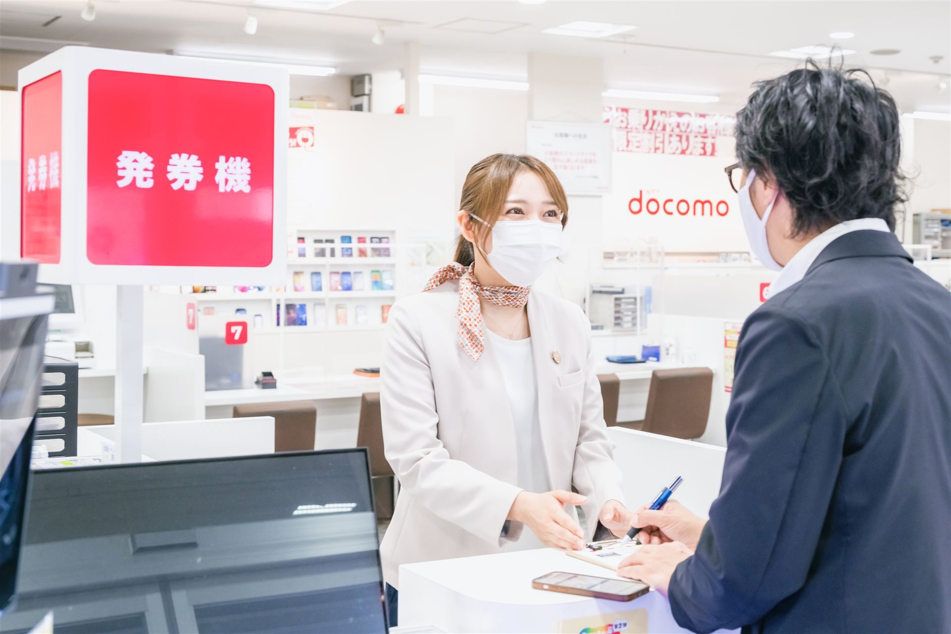 ドコモショップのカウンターでお客様を案内するスタッフ